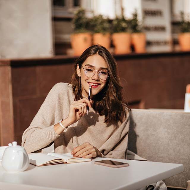 pretty-young-student-girl-with-dark-wavy-hairstyle-trendy-makeup-glasses-beige-pullover-studying-city-cafe-terrace-autumn-warm-day